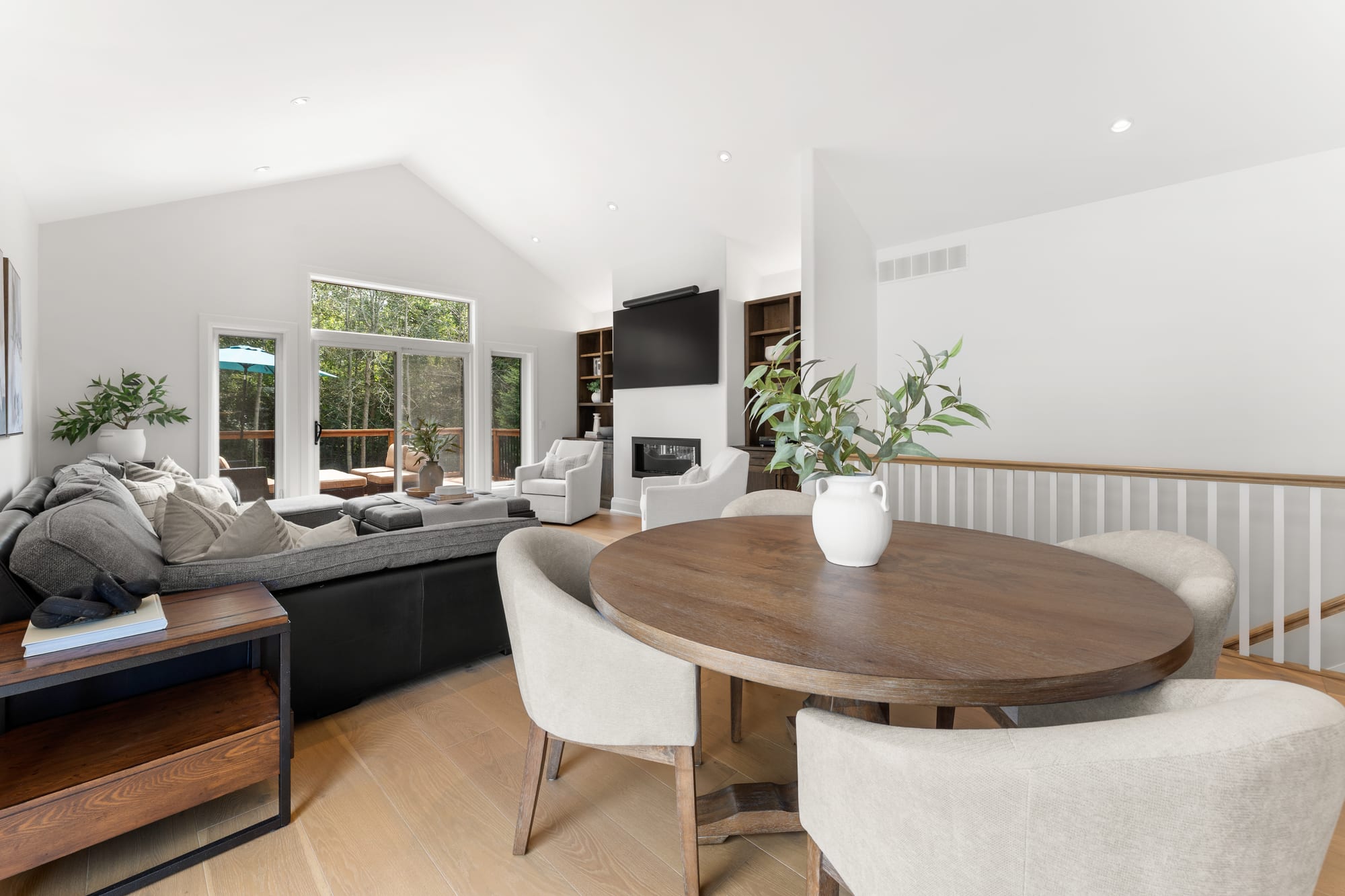 Round dining table beside the great room sectional, with the gas fireplace and deck doors beyond