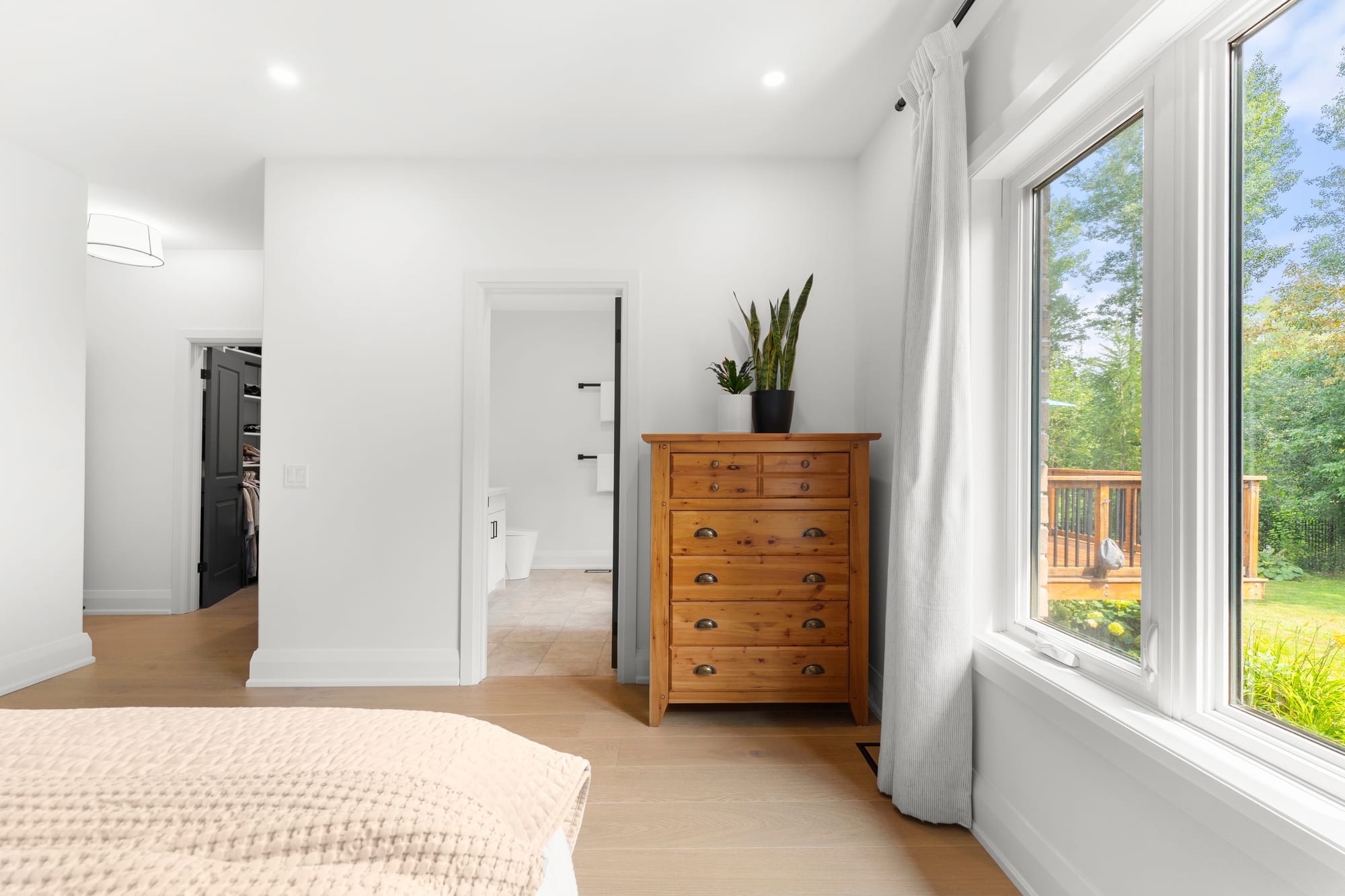 Primary bedroom looking toward the walk-in closet and ensuite doors, with a window onto the rear deck and yard