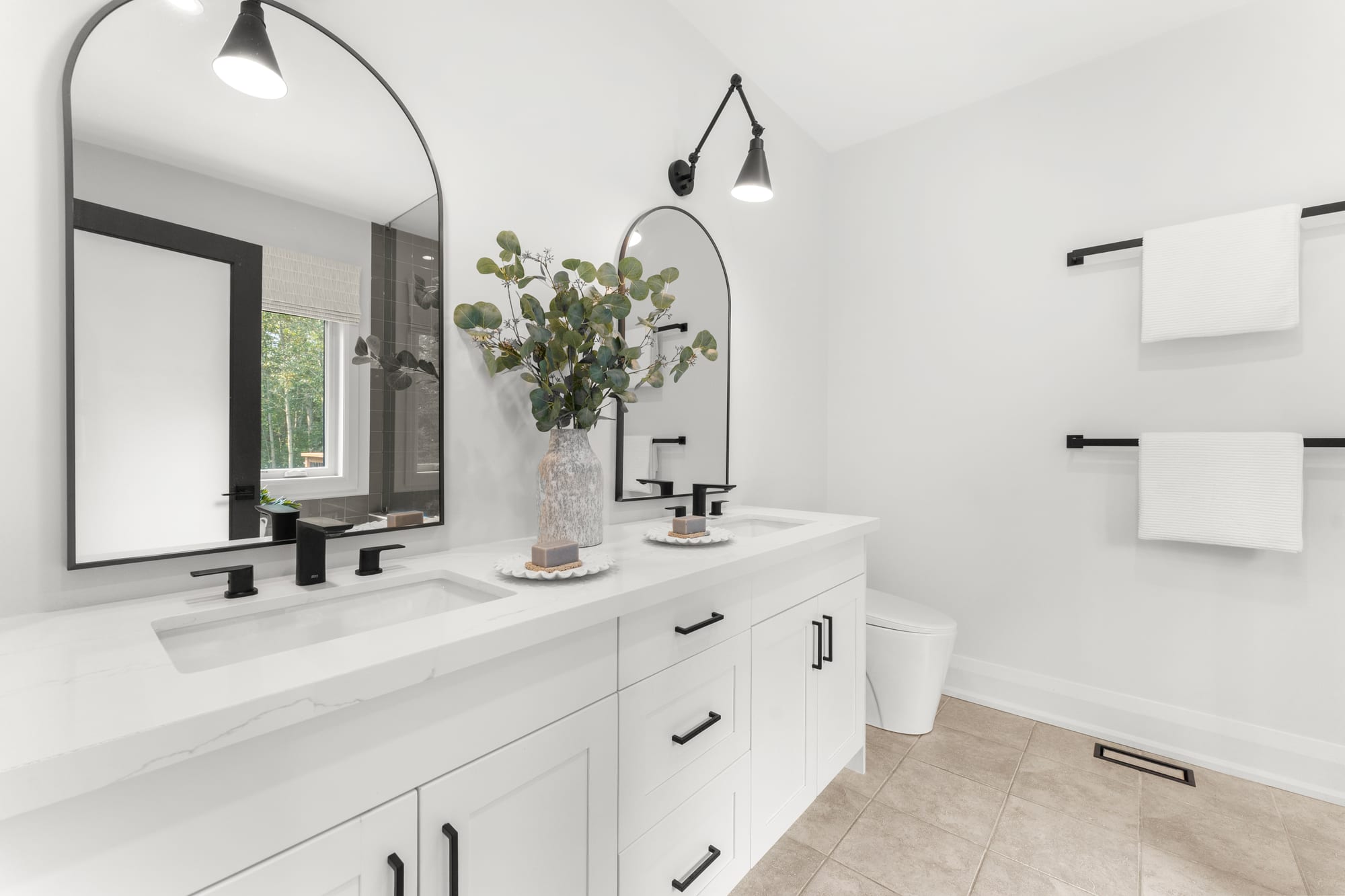 Ensuite double vanity with quartz counter, arched black-framed mirrors and matte black fixtures