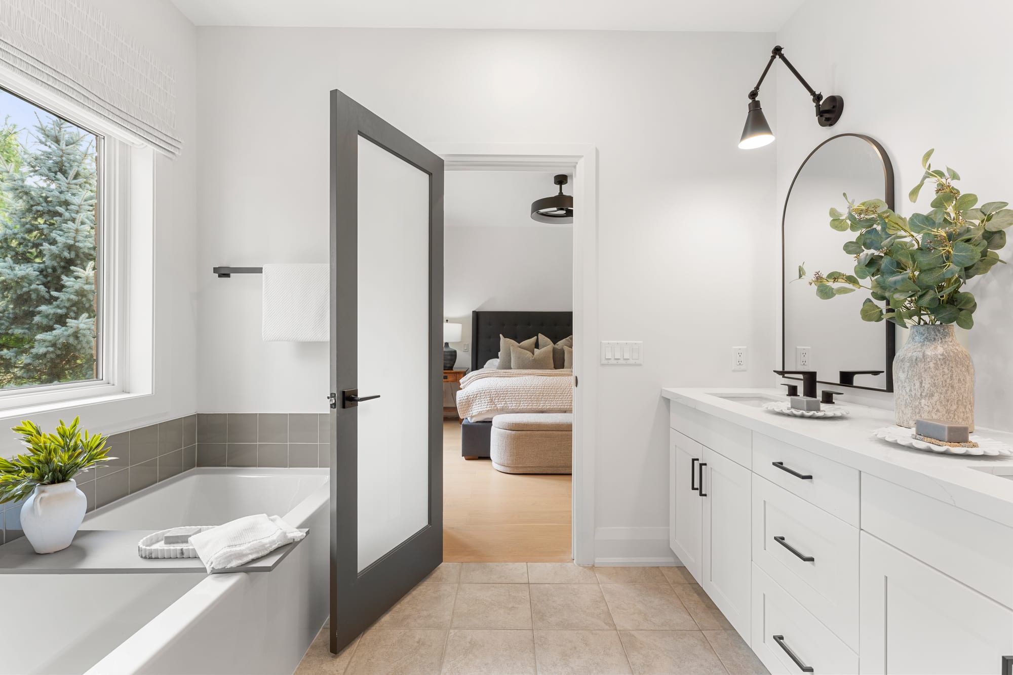 Ensuite looking through the frosted glass door to the primary bedroom, soaker tub on the left and double vanity on the right