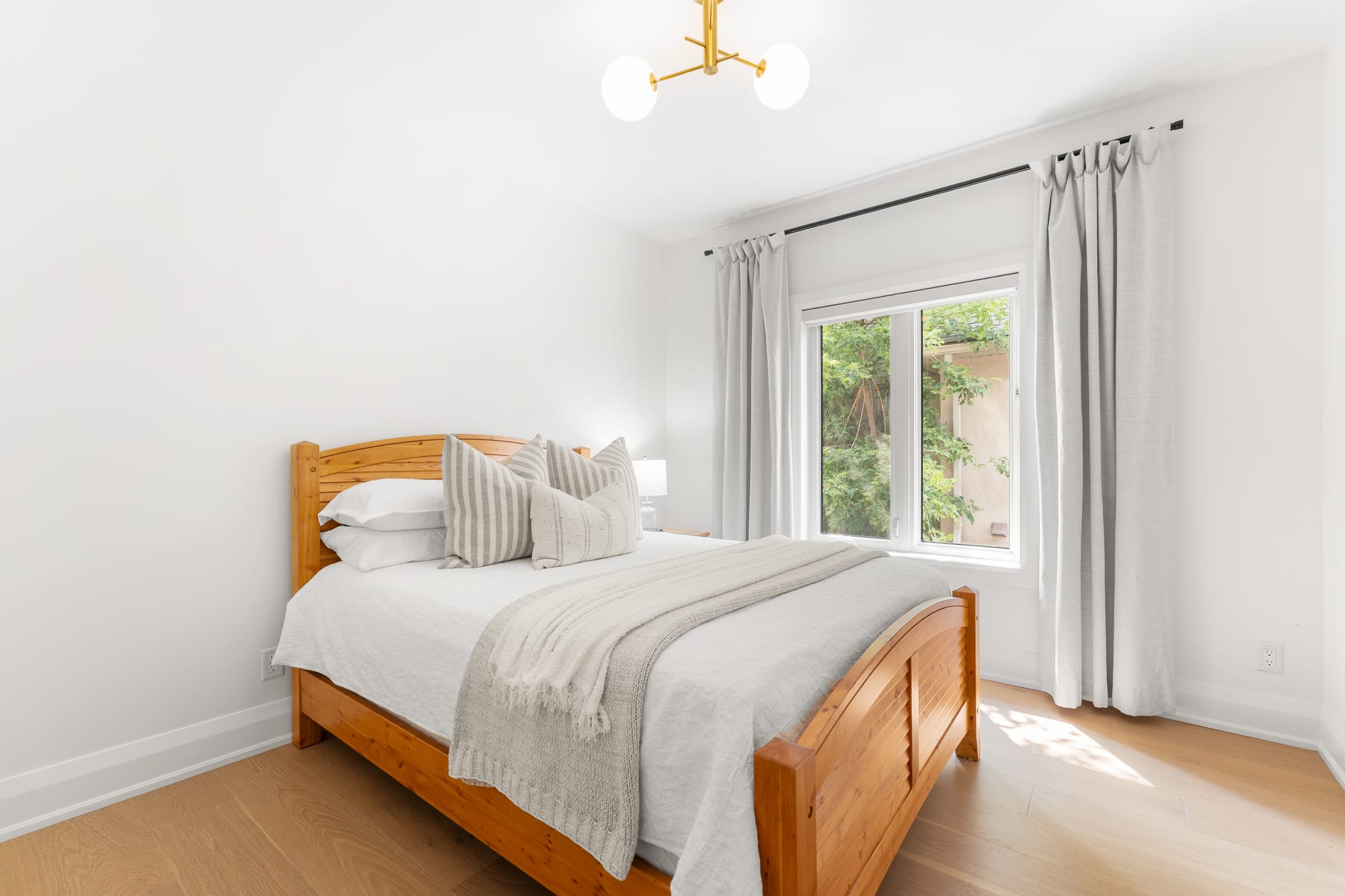 Main-floor guest bedroom with a pine bed frame, brass globe light fixture and a garden view