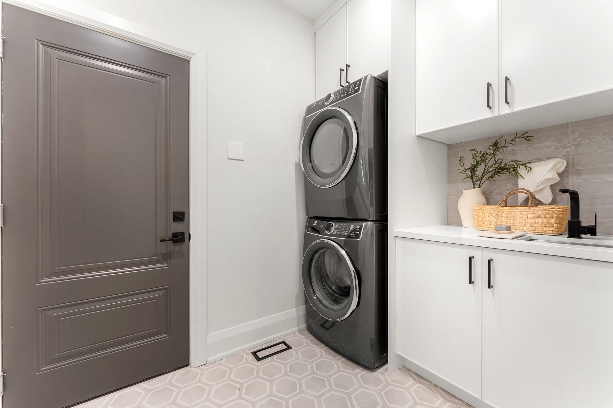 Main-floor laundry and mudroom with stacked washer and dryer, quartz-topped sink counter and hexagon tile floor