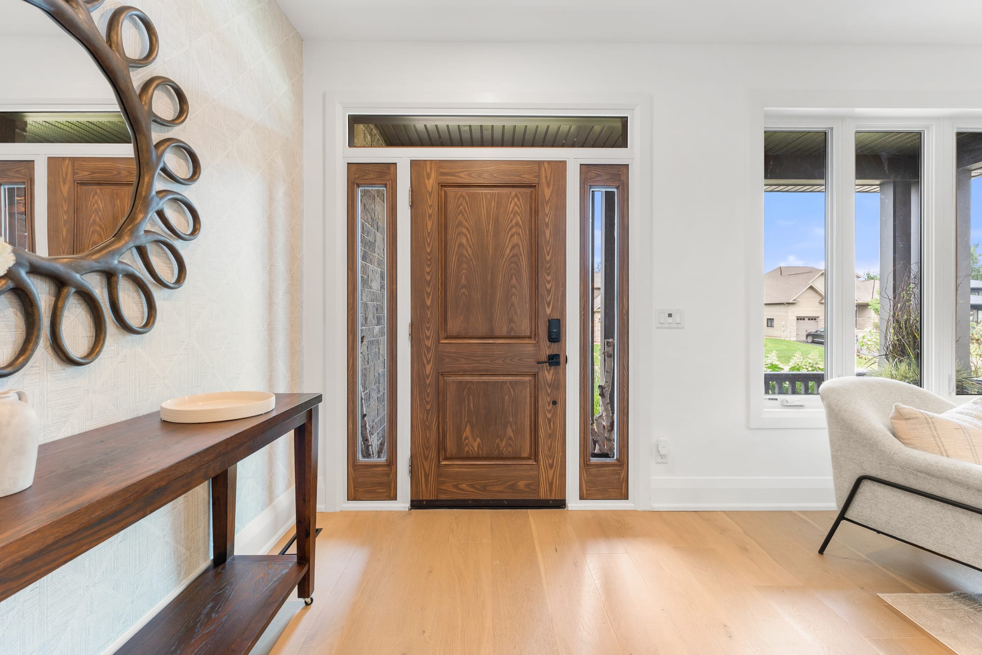 Front foyer with white oak floors, a solid wood entry door with sidelights, and a sunburst mirror above a console table