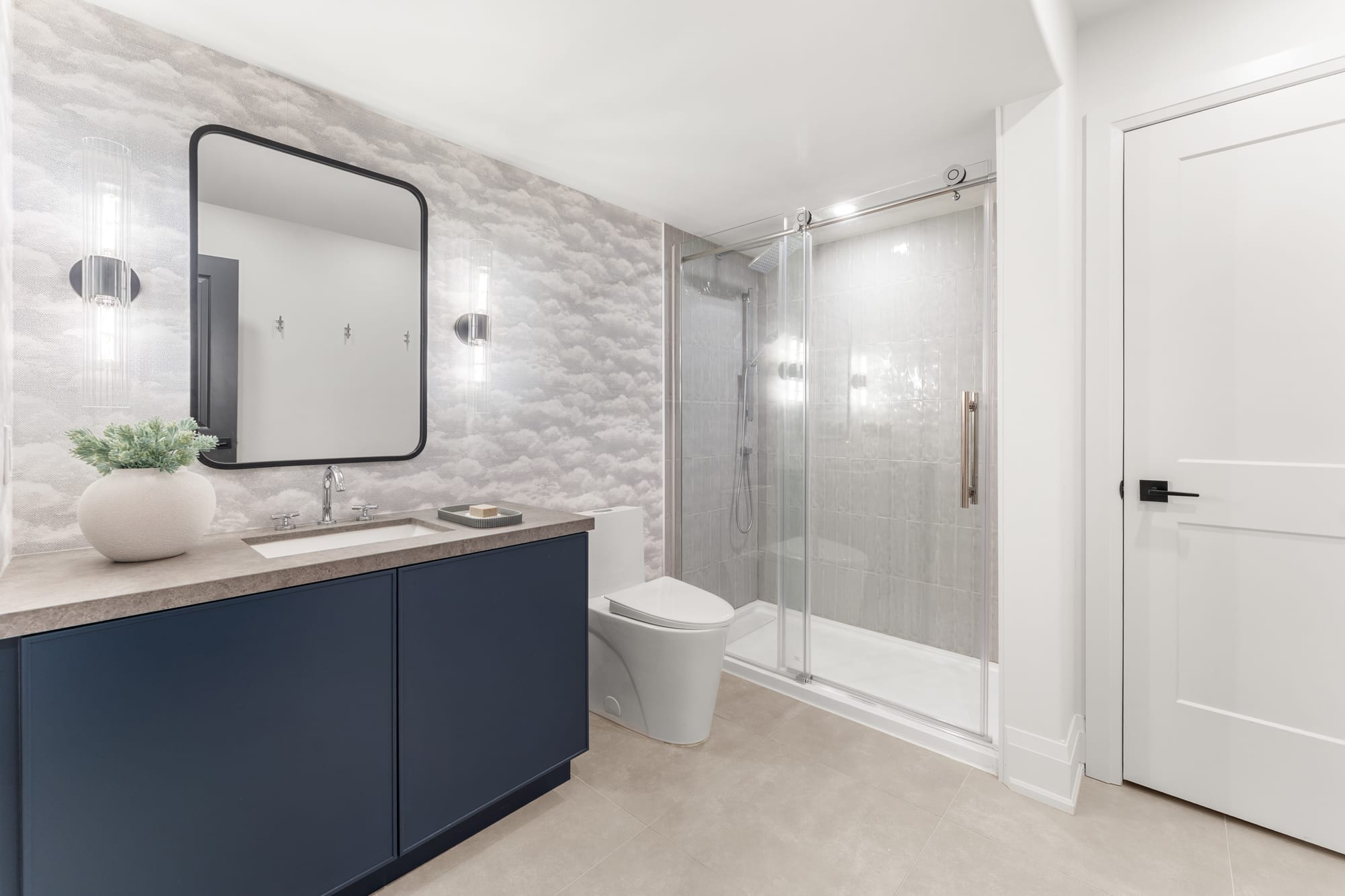 Lower-level three-piece bathroom with a navy vanity, cloud-print wallpaper and a glass sliding shower