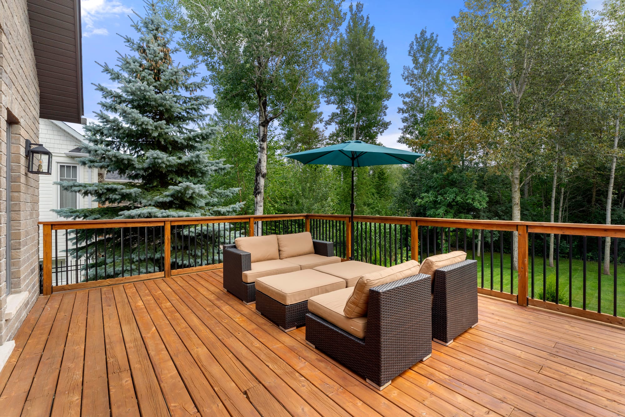 South-facing cedar deck with wicker lounge seating and an umbrella, backing onto mature trees
